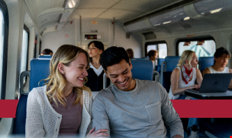 A Metrolink car full of passengers with a main focus on a couple sitting together and a banner colored in San Bernardino Red in the back.